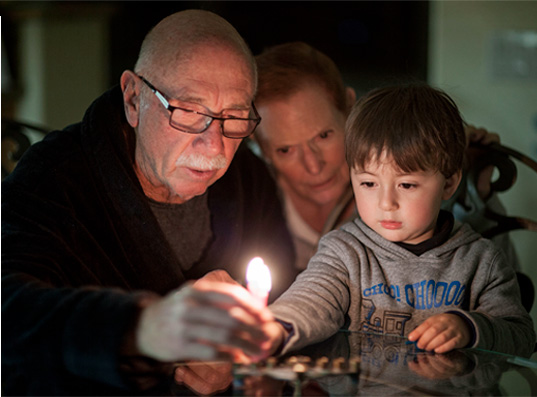 Niño y sus abuelos contemplando una vela de cumpleaños encendida en primer plano